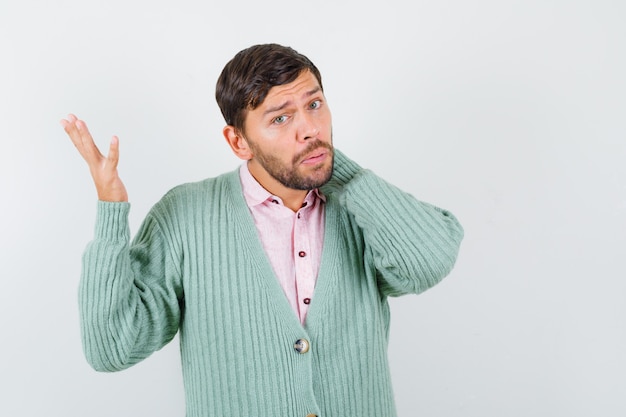 Jonge man met hand op nek, hand opstekend in shirt, vest en verbaasd kijkend. vooraanzicht.