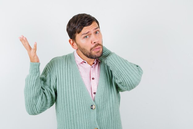 Jonge man met hand op nek, hand opstekend in shirt, vest en verbaasd kijkend. vooraanzicht.