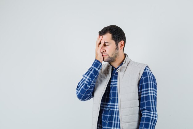 Jonge man met hand op zijn gezicht in shirt, mouwloos jasje en op zoek moe, vooraanzicht. ruimte voor tekst