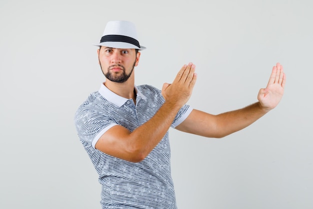 Jonge man met hoed, gestreept t-shirt die de armen preventief opheft en er flexibel uitziet, vooraanzicht.