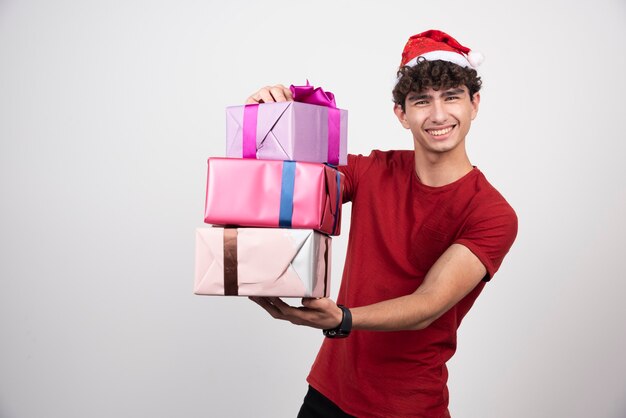 Jonge man met kerstmuts die zich gelukkig voelt en geschenken vasthoudt.