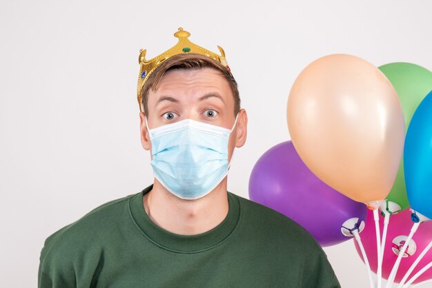 Gratis foto jonge man met kleurrijke ballonnen in masker op wit