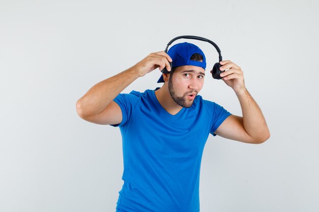 Jonge man met koptelefoon in blauw t-shirt en pet vooraanzicht.