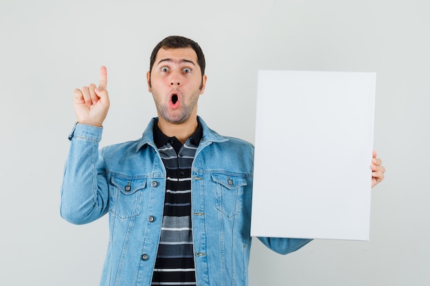 Jonge man met leeg canvas, omhoog in t-shirt, jasje en nieuwsgierig kijken