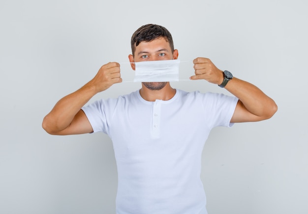 Jonge man met medisch masker over zijn mond in wit t-shirt, vooraanzicht.