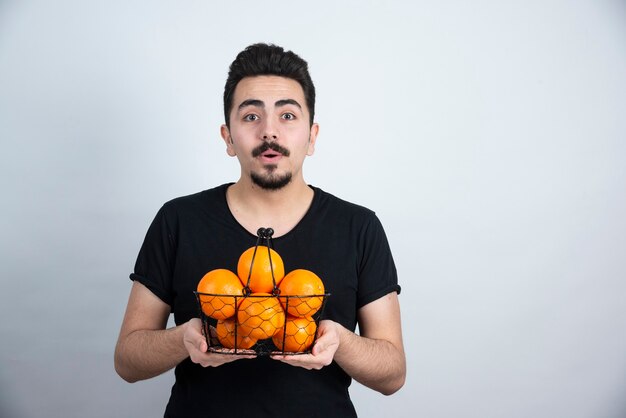 jonge man met metalen mand vol oranje fruit.