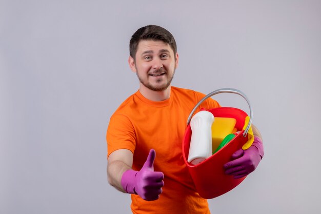 Jonge man met oranje t-shirt en rubberen handschoenen met emmer met reinigingsgereedschap