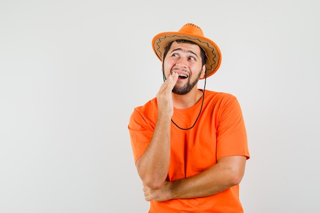 Jonge man met pijnlijke tand in oranje t-shirt, hoed en ongemakkelijk, vooraanzicht.