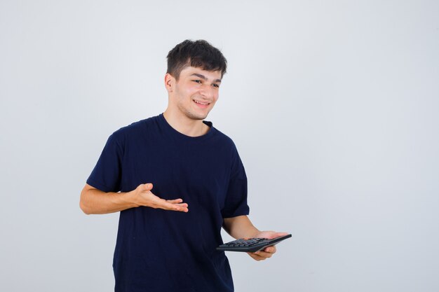 Jonge man met rekenmachine in zwart t-shirt en op zoek vrolijk. vooraanzicht.