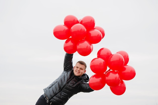 Jonge man met rode ballonnen in zijn handen. het concept voor sint-valentijn Premium Foto