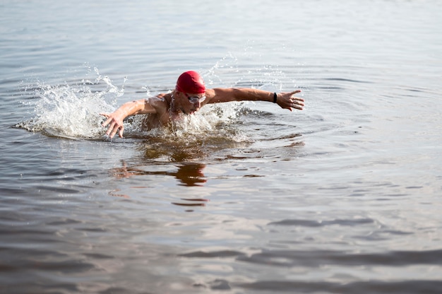 Gratis foto jonge man met rode dop zwemmen in meer