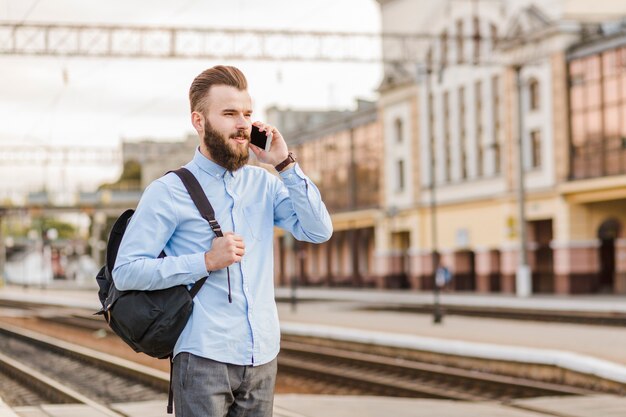 Jonge man met rugzak praten op mobiel bij treinstation