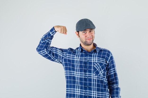 Jonge man met spieren, knipogen oog in shirt, pet en op zoek zelfverzekerd. vooraanzicht.