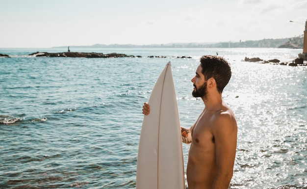 Jonge man met surfplank op de wal in de buurt van water