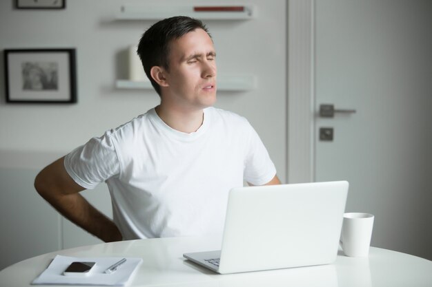 Jonge man met zijn handen aan zijn rug, strekt na het werken op laptop