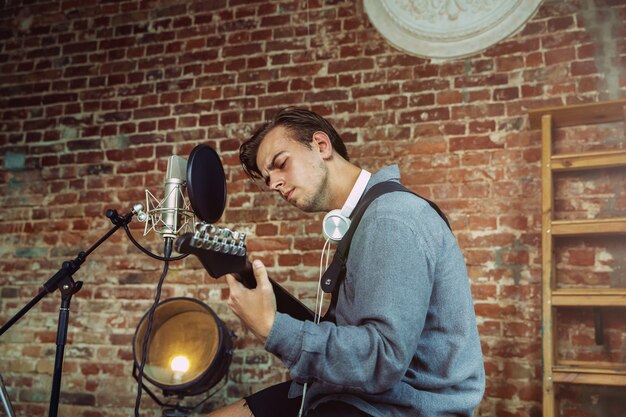 Jonge man muziek opnemen, gitaar spelen en thuis zingen