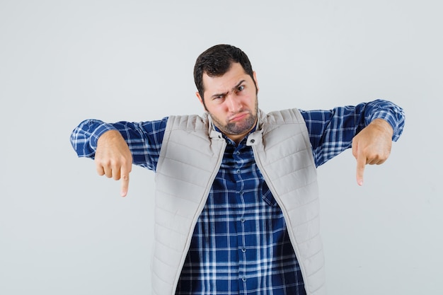 Jonge man naar beneden in shirt, mouwloos jasje en op zoek agressief. vooraanzicht.