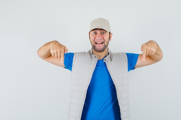 Jonge man naar beneden in t-shirt, jasje, pet en op zoek vrolijk. vooraanzicht.