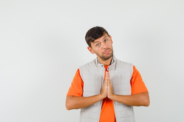 Jonge man namaste gebaar in t-shirt, jasje en op zoek nederig.