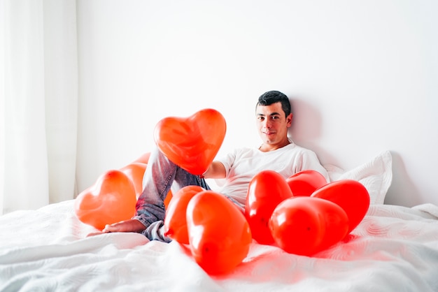 Jonge man op bed tussen ballonnen in de vorm van harten