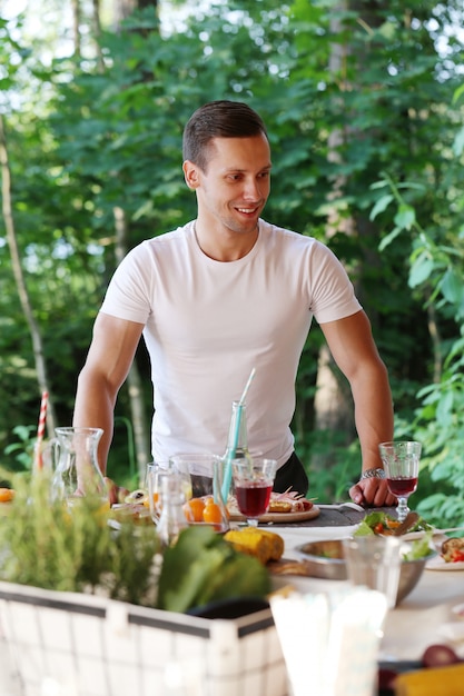 Jonge man op een worst en maïs op de grill