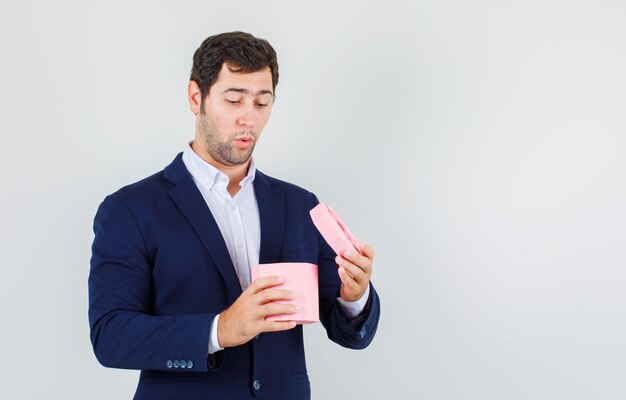 Jonge man op zoek naar geopende geschenkdoos in pak en op zoek verrast. vooraanzicht.