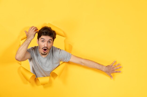 Jonge man op zoek van gescheurde gele papieren achtergrond indoor man gezichtsuitverkoop