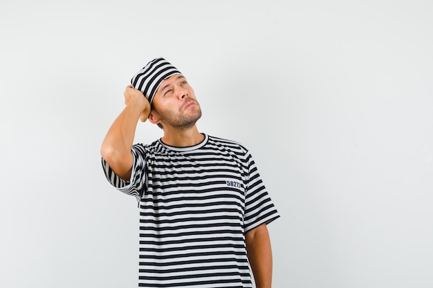 Jonge man opzoeken met de hand op het hoofd in gestreepte t-shirt hoed en peinzend kijken