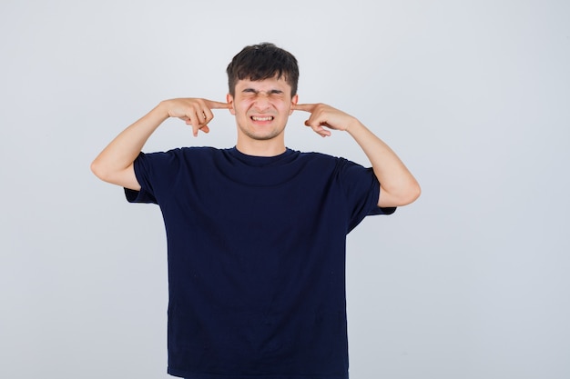 Jonge man oren met vingers in zwart t-shirt plug en op zoek geërgerd, vooraanzicht.