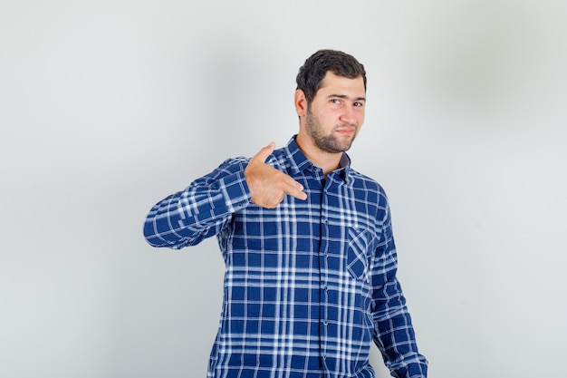 jonge man pistool gebaar in ingecheckte shirt tonen en op zoek zelfverzekerd.