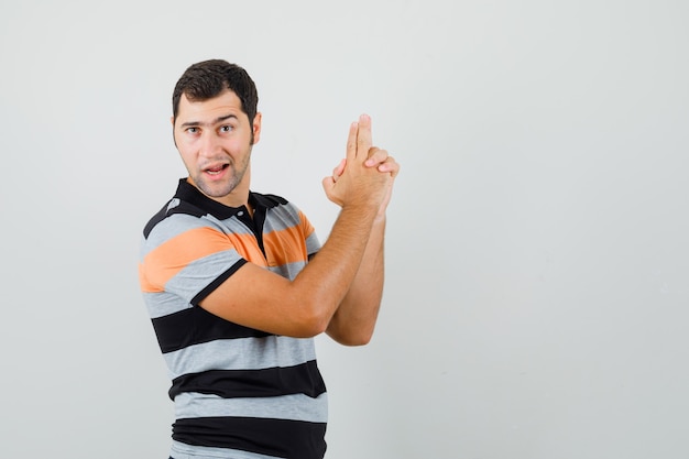 Jonge man pistool gebaar in t-shirt tonen en er zeker van kijken. vooraanzicht. ruimte voor tekst