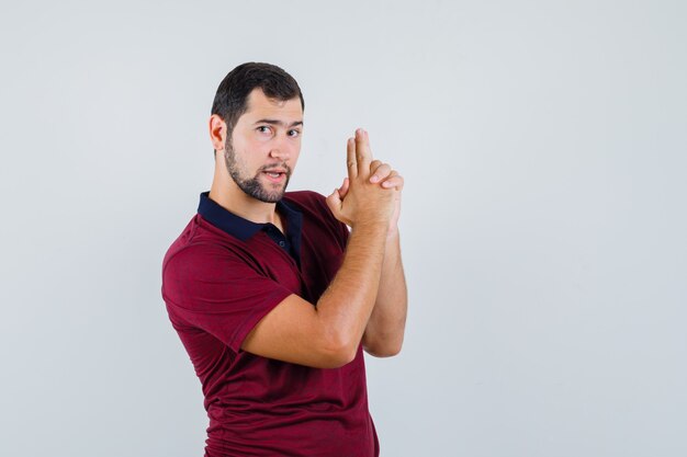 Jonge man pistool teken in rode t-shirt tonen en klaar, vooraanzicht kijken.