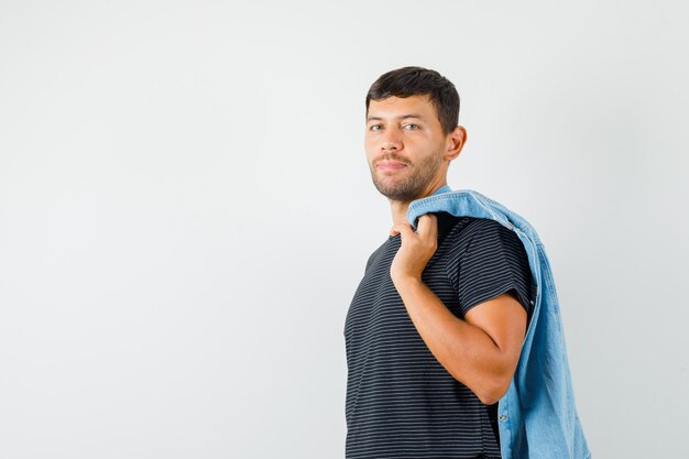 Jonge man poseren terwijl jasje op de rug in t-shirt en ziet er knap uit