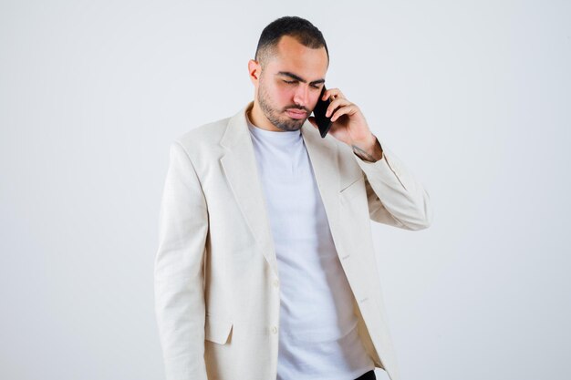 Jonge man praat met de telefoon in wit t-shirt, jas en ziet er serieus uit. vooraanzicht.