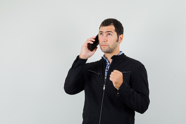 Jonge man praten op mobiele telefoon in shirt, jasje en peinzend, vooraanzicht kijken.