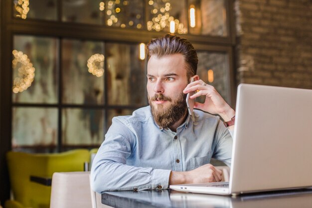 Jonge man praten op mobiele telefoon met laptop op Bureau