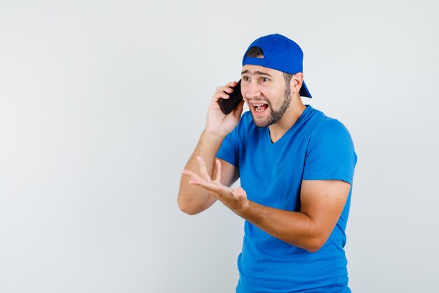 Jonge man praten over de mobiele telefoon in blauw t-shirt en pet en op zoek opgewonden