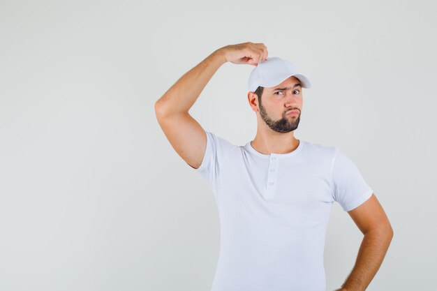 Jonge man raakt op zijn pet in t-shirt, pet en ziet er grappig uit. vooraanzicht.