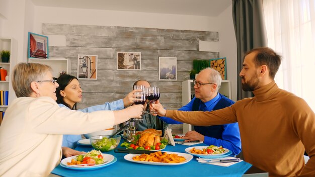 Jonge man rammelende een glas wijn met zijn familie terwijl u geniet van het diner.