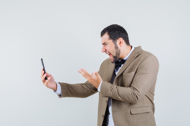 Jonge man schreeuwen op video-chat in pak en kijkt boos. vooraanzicht.