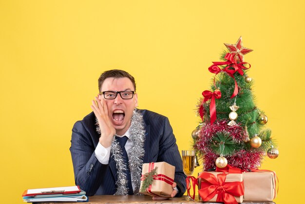 jonge man schreeuwen tegen iemand die aan de tafel zit in de buurt van de kerstboom en presenteert op geel