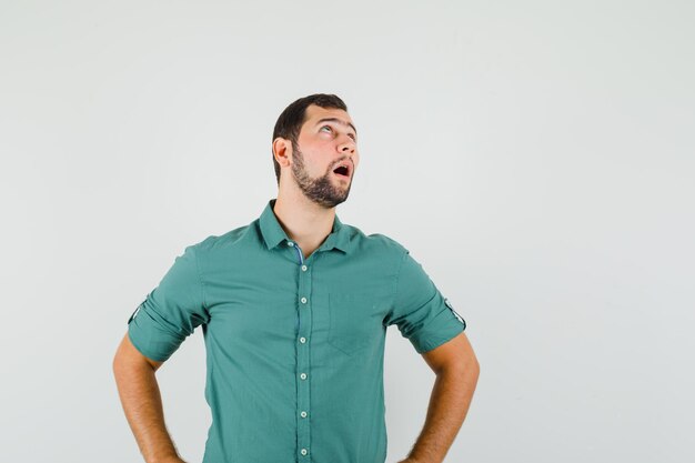 Jonge man staat terwijl hij opzij kijkt in een groen shirt en er verveeld uitziet. vooraanzicht.