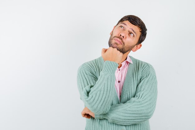 Jonge man steunt kin op vuist, kijkt omhoog in shirt, vest en kijkt peinzend. vooraanzicht.