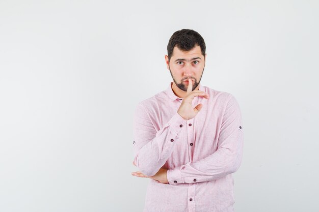 Jonge man stilte gebaar in roze shirt tonen en voorzichtig kijken