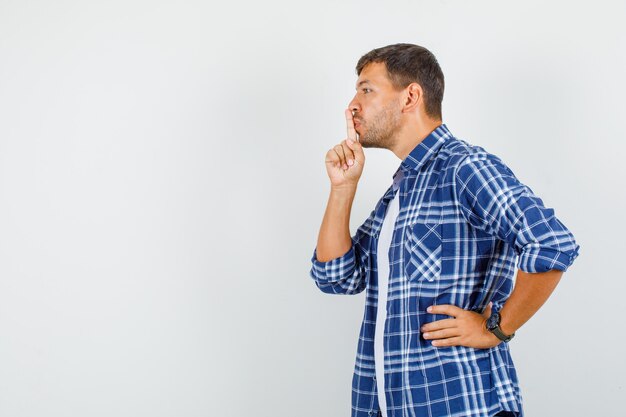 Jonge man stilte gebaar met hand op taille in shirt tonen en voorzichtig kijken. .