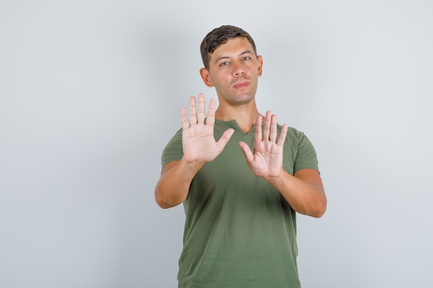 Jonge man stop gebaar in leger groen t-shirt vooraanzicht tonen.