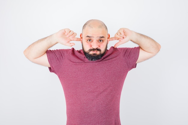 Jonge man stopt oren met vingers terwijl hij zijn wangen puffend in roze t-shirt vooraanzicht.