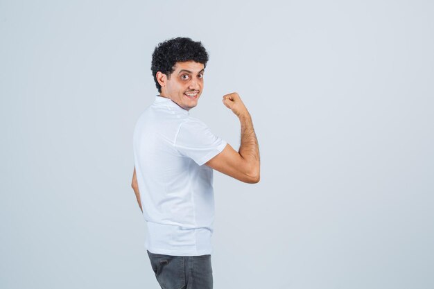 Jonge man toont armspieren in wit t-shirt, broek en ziet er zelfverzekerd uit. .