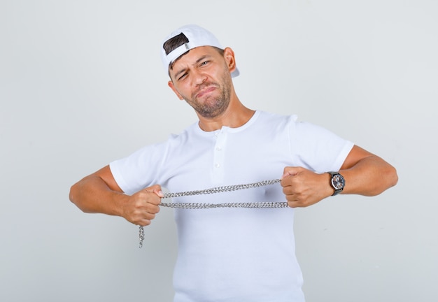 Gratis foto jonge man trekt metalen ketting in wit t-shirt, pet, vooraanzicht.