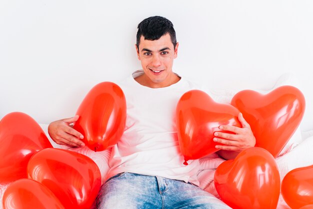 Jonge man tussen ballonnen in de vorm van harten